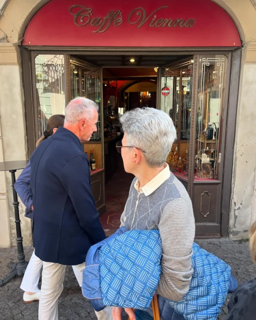 People at the entrance of Caffe Vienna with an ornate red and gold sign, captured during the daytime.
