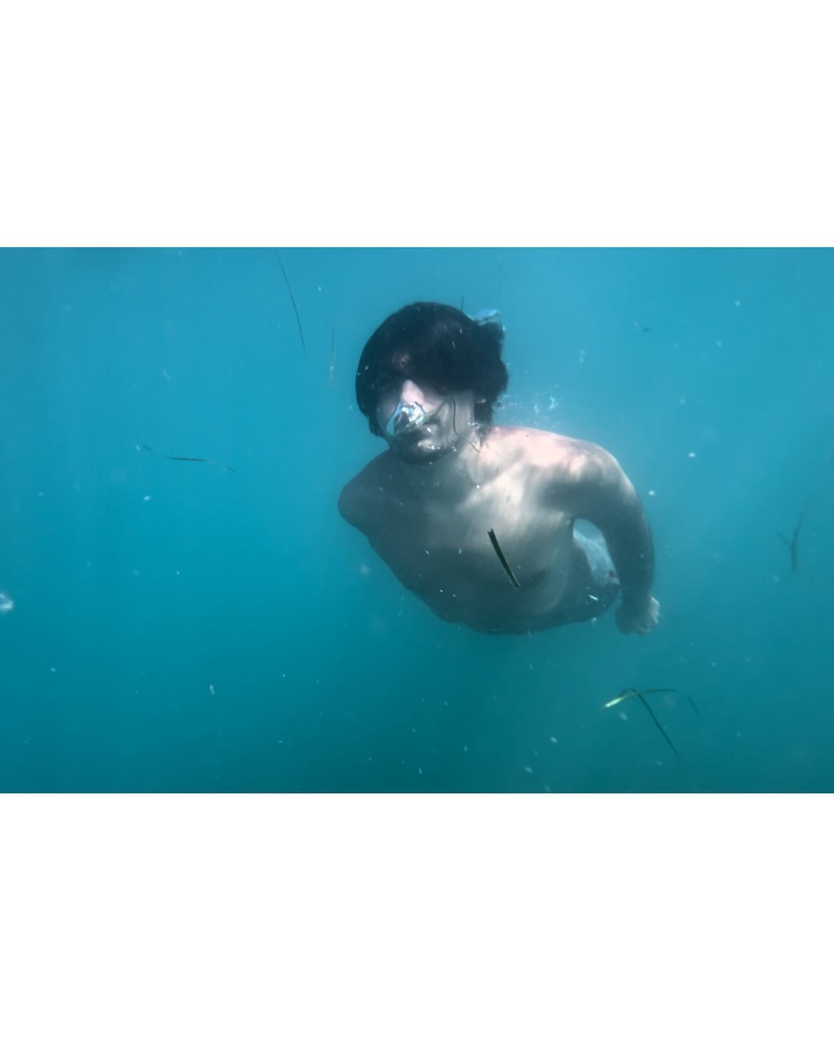 Underwater view of a young adult male swimming in clear turquoise water, his face partially visible with bubbles around him.