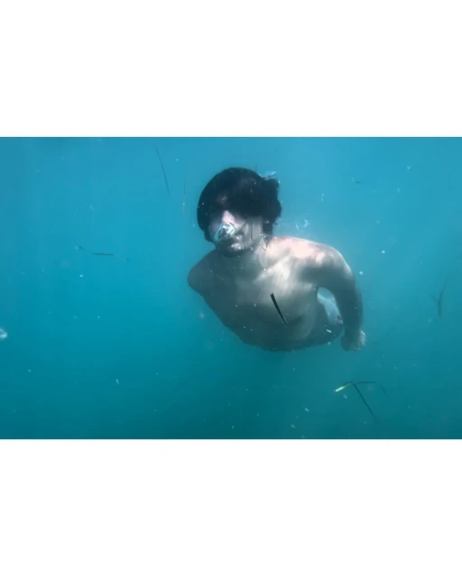 Underwater view of a young adult male swimming in clear turquoise water, his face partially visible with bubbles around him.