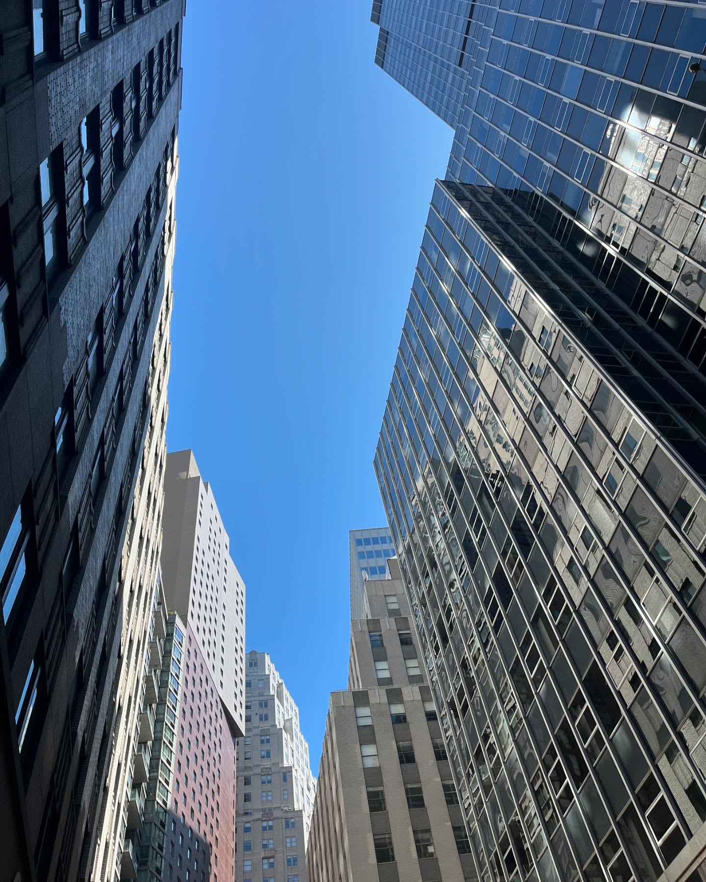 Upward angle view of modern buildings against a clear blue sky in a cityscape, showcasing contemporary architecture.