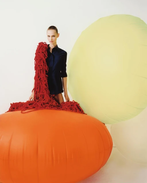 Fashion shot of a model posing with bright oversized balloons, wearing a dark shirt, and red tangled ropes in a brightly lit studio.