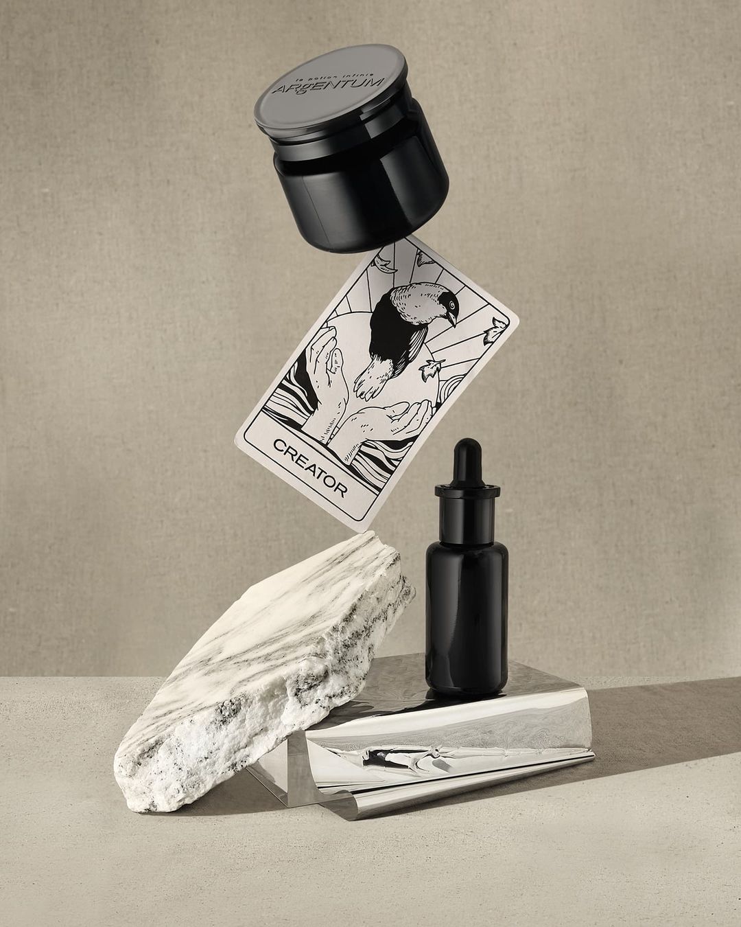 Still life featuring Argentum skincare jar and bottle, creator card, and marble stone, creating a modern and luxurious product shot.