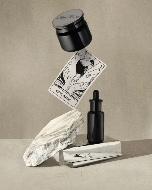 Still life featuring Argentum skincare jar and bottle, creator card, and marble stone, creating a modern and luxurious product shot.