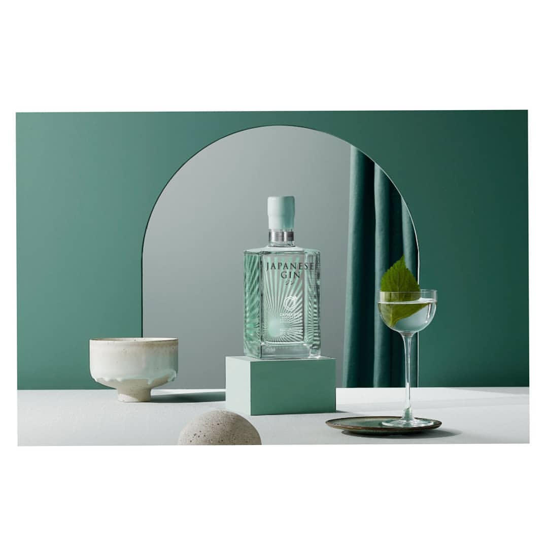 Japanese gin bottle on display with cocktail glass, minimalist shapes, and a cool color palette in a studio setting.