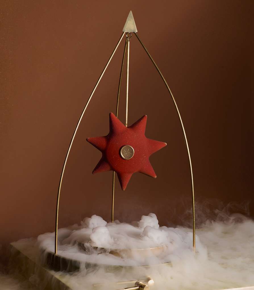 Red star-shaped object on a gold metal frame, centered over a white smoky base against a gradient brown background, creating an artistic, unique display.