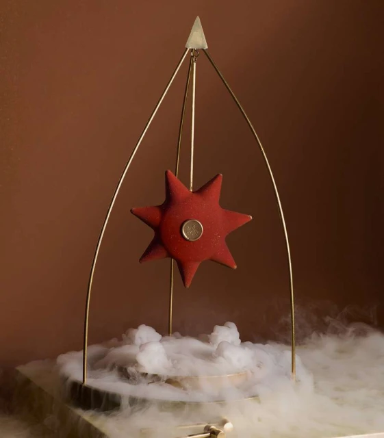 Red star-shaped object on a gold metal frame, centered over a white smoky base against a gradient brown background, creating an artistic, unique display.
