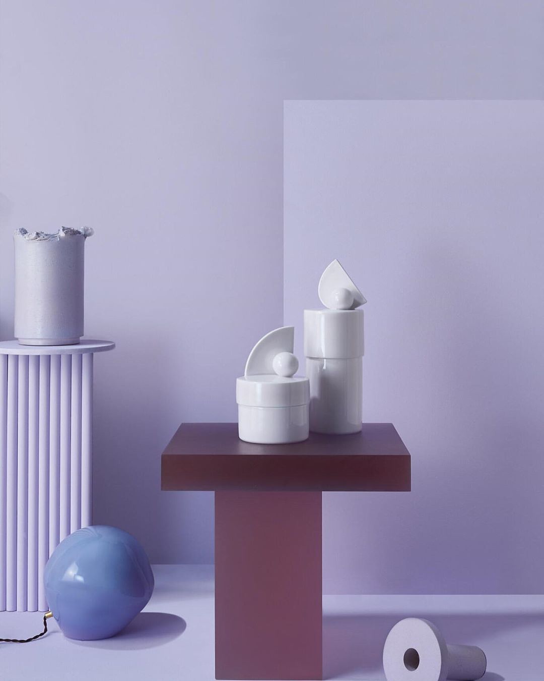 Still life with geometric ceramic shapes and platforms in light purple studio. Modern, minimalist composition with cylinders and spheres.