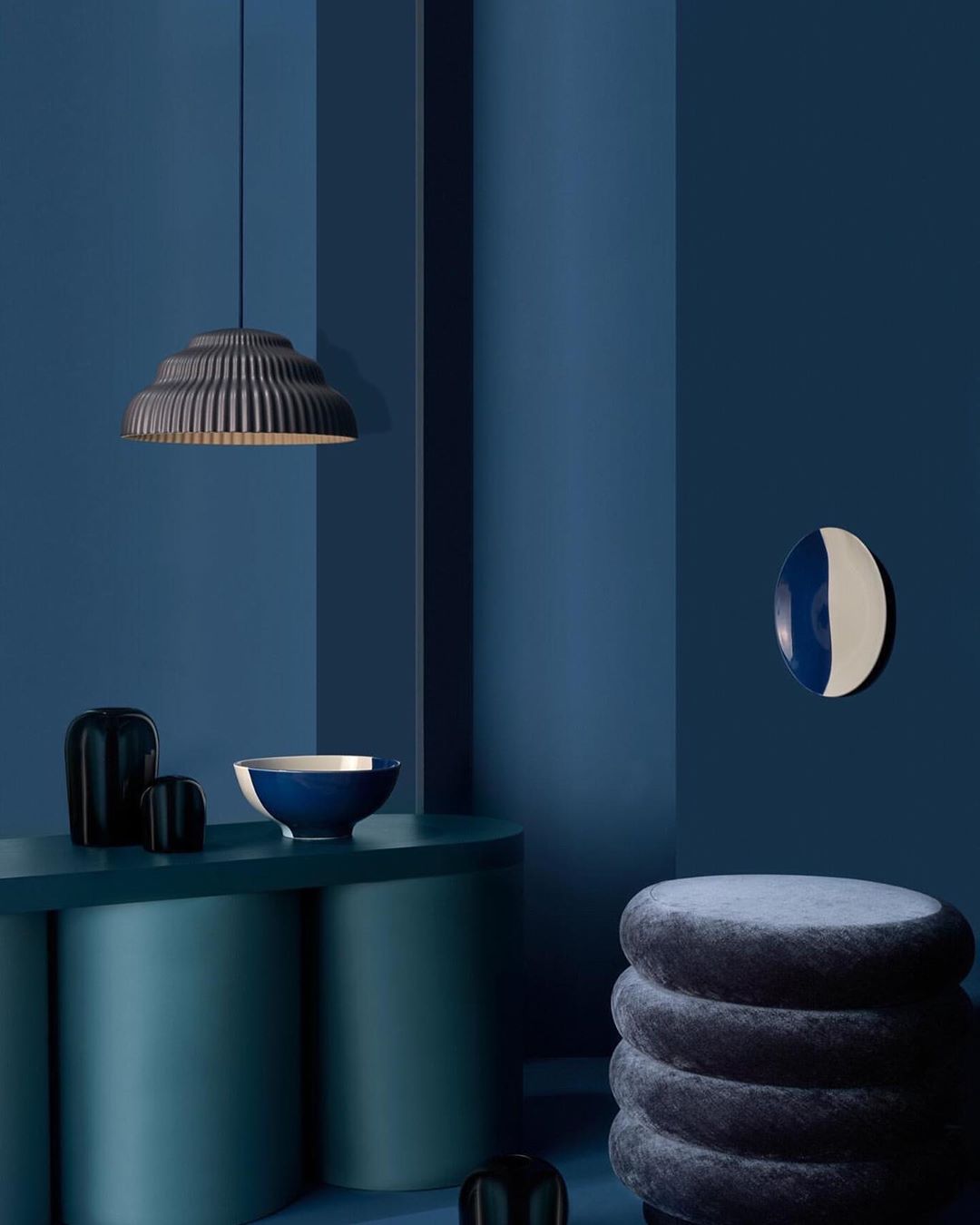 Interior design scene features a hanging pendant lamp, vases, a bowl, and a decorative disc in a room with teal and blue walls.