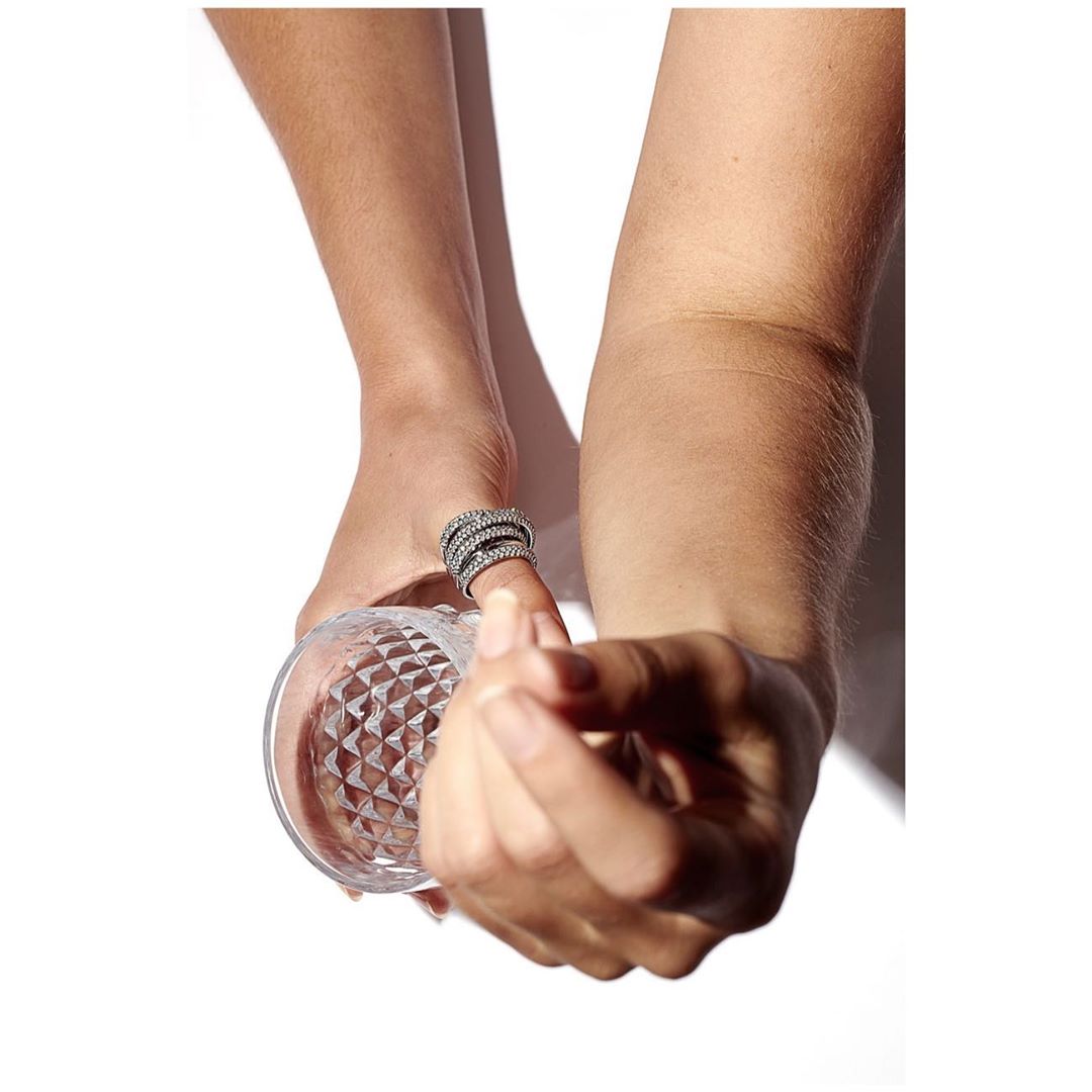 Close-up shot of a woman's hands holding a textured glass, accentuating a diamond-studded ring on her finger against a white backdrop.