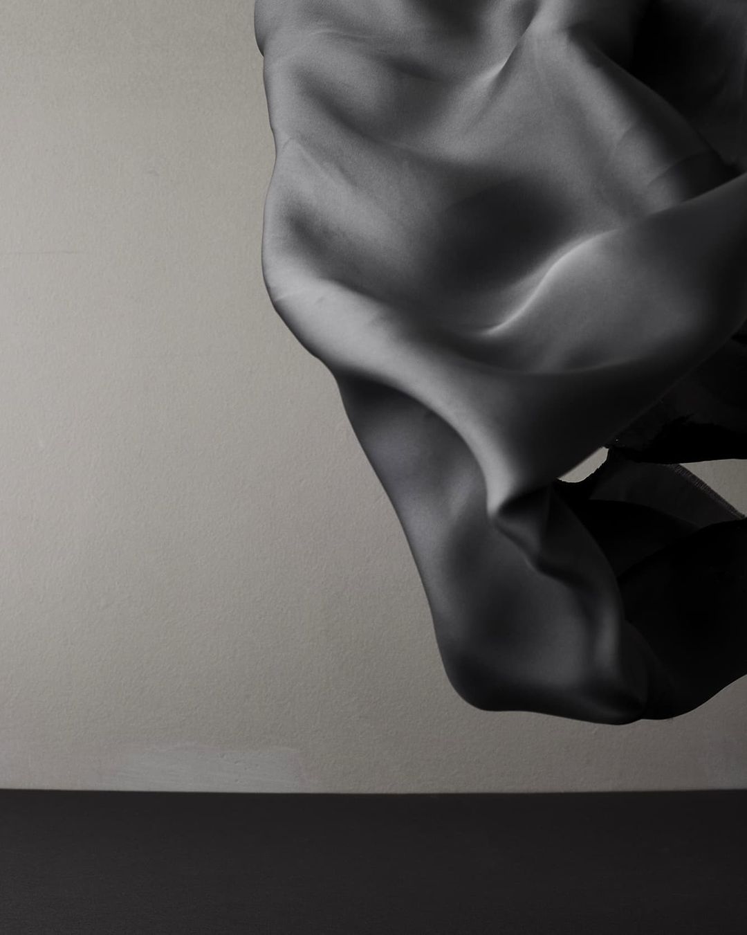 Elegant, draped fabric flowing against a neutral backdrop with a dark base. Minimalist composition showcasing texture and form.