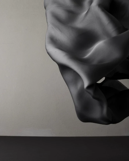 Elegant, draped fabric flowing against a neutral backdrop with a dark base. Minimalist composition showcasing texture and form.