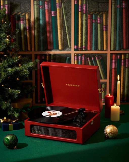 Red Crosley record player on a green table with Christmas decor and a vintage bookshelf backdrop, creating a cozy, festive atmosphere.
