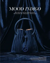 Deep blue suede bucket handbag with round handle centered on a dark blue velvet draped fabric background