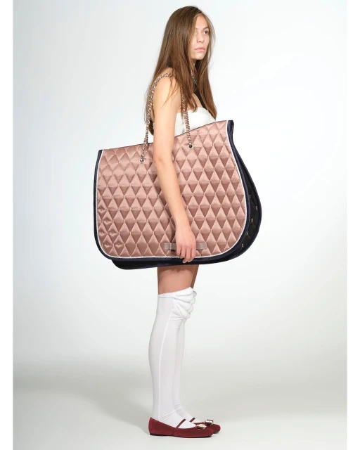 A young female model strikes a pose against a neutral backdrop, showcasing an oversized, quilted tote bag with chain straps.