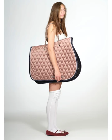 A young female model strikes a pose against a neutral backdrop, showcasing an oversized, quilted tote bag with chain straps.