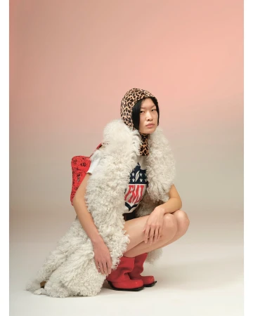 Portrait of a crouched Asian woman in a white t-shirt, red boots, and an animal print headscarf against a light gradient background.