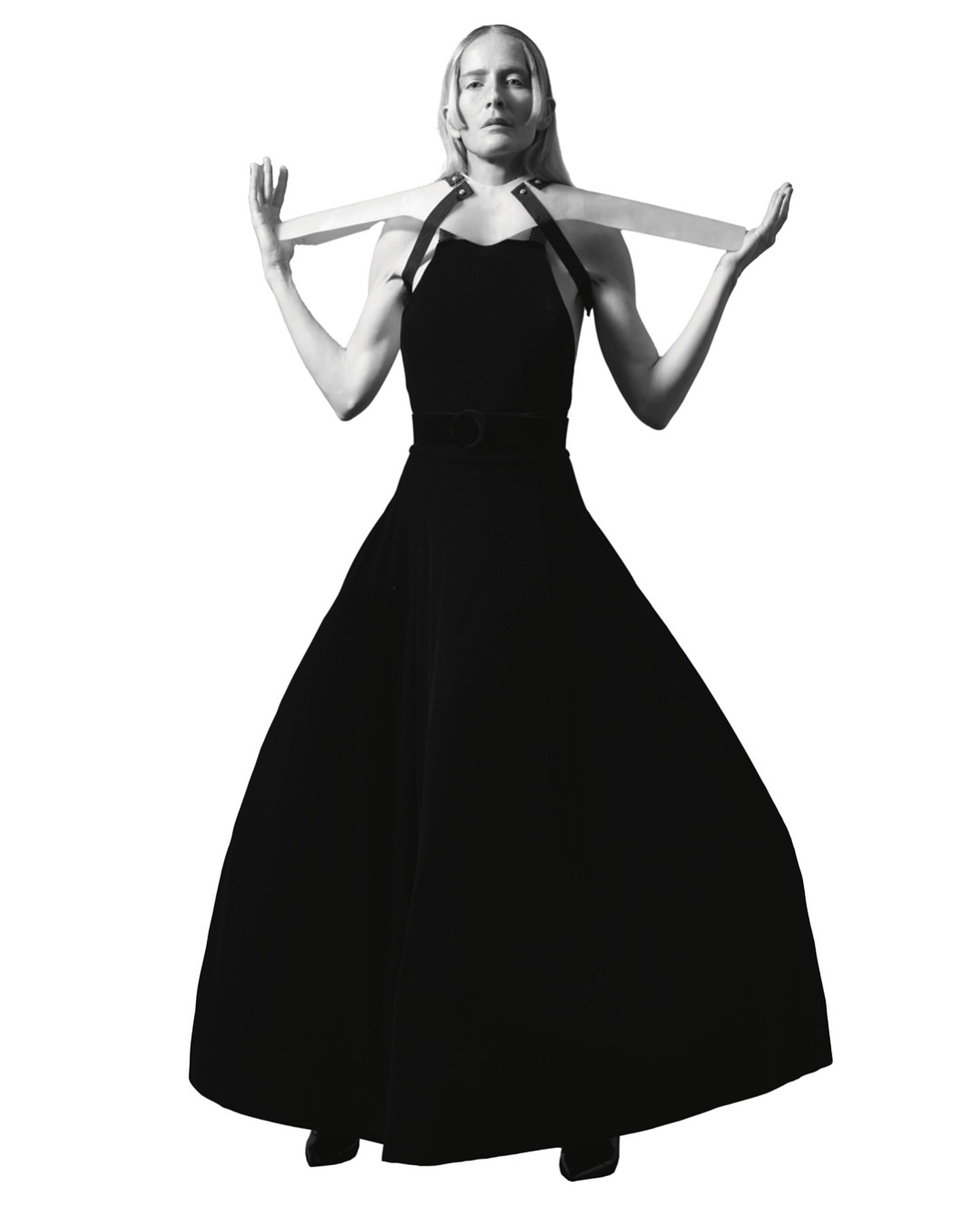 Monochrome studio shot of an adult woman wearing a black gown, holding a wooden structure against a plain white backdrop.