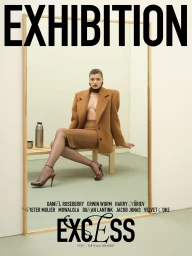 Model seated on a wooden bench in an oversized camel blazer and skirt, framed inside a large wooden mirror.