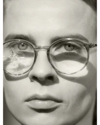 Close-up portrait of a person wearing round glasses with a cracked lens, captured by Anuschka Blommers and Niels Schumm.
