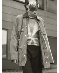 Model wearing a mirrored visor mask and textured jacket over a patterned turtleneck outside a building in Paris.