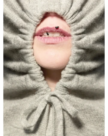 Close-up of a person wearing a gathered grey knit hood with small insects on their lips, photographed by Anuschka Blommers & Niels Schumm