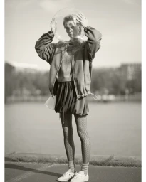 Model holding a transparent helmet over their head wearing a zip jacket and patterned tights outdoors.