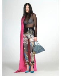 Model wearing sheer black top, patterned leggings, and a draped pink cape holding a blue handbag against a white background