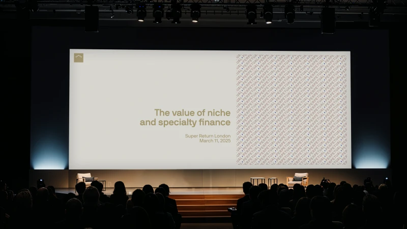 Wide conference stage with a large presentation screen reading The value of niche and specialty finance before a seated audience