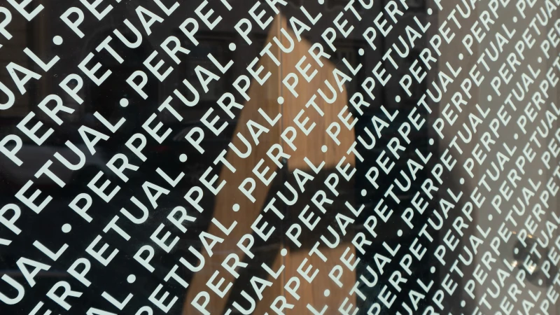 Close-up angled shot of dark glass surface featuring repeated white typographic text reading PERPETUAL with dot separators