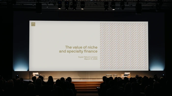 Wide conference stage with a large presentation screen reading The value of niche and specialty finance before a seated audience