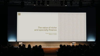 Wide conference stage with a large presentation screen reading The value of niche and specialty finance before a seated audience