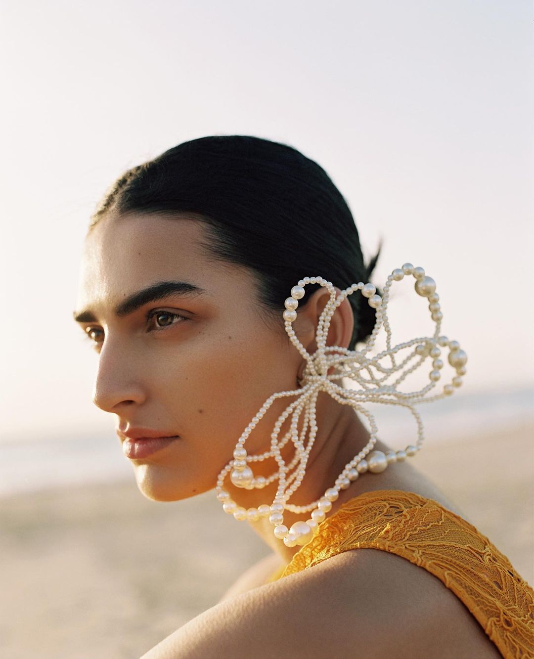 Close-up of a woman wearing a yellow top and beaded floral earring, showcasing fashion, beauty, and portrait photography.