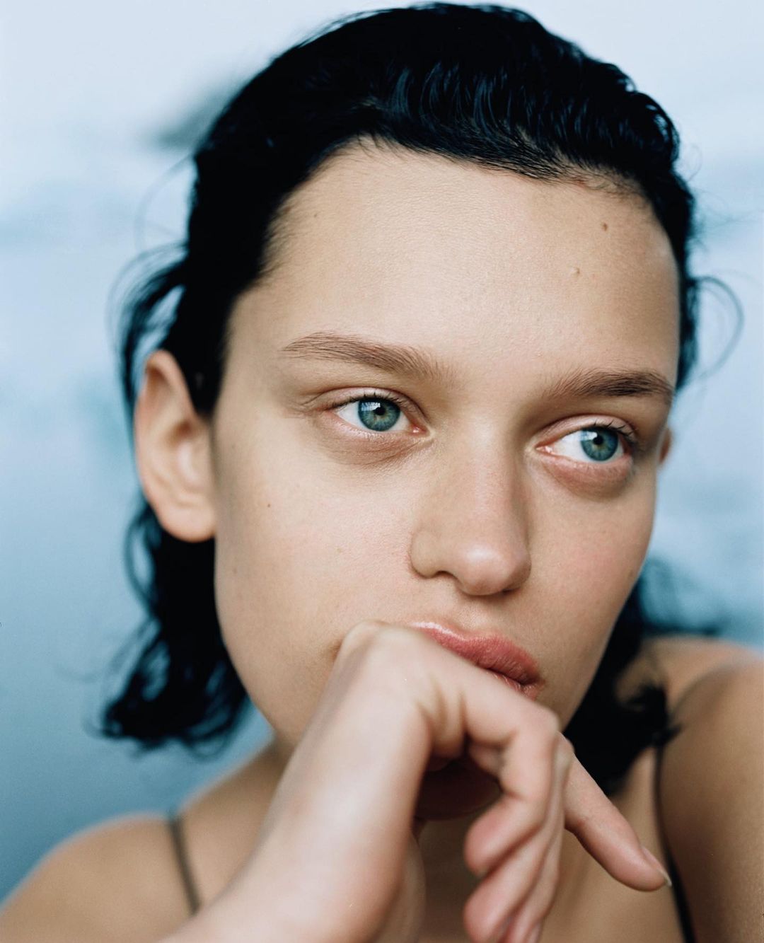 Portrait of an adult woman with short dark hair and fair skin looking off to the side with hand near her lips in a contemplative pose.