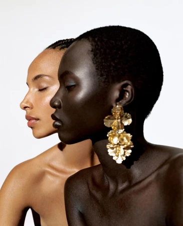 Close-up profile portrait of two women with eyes closed against a bright white background wearing large gold earrings