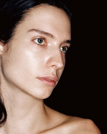 Portrait of a young fair-skinned woman with dark hair against a black background, looking off to the side with a serene expression.