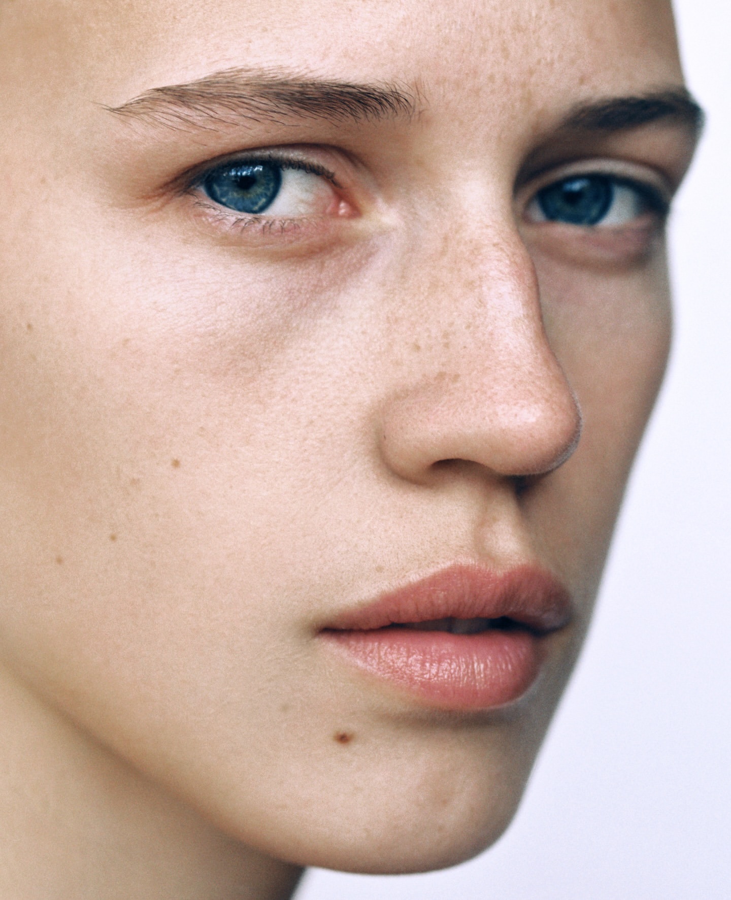 Close-up portrait of a woman with vibrant blue eyes, freckles, and natural skin texture photographed by Anya Holdstock.