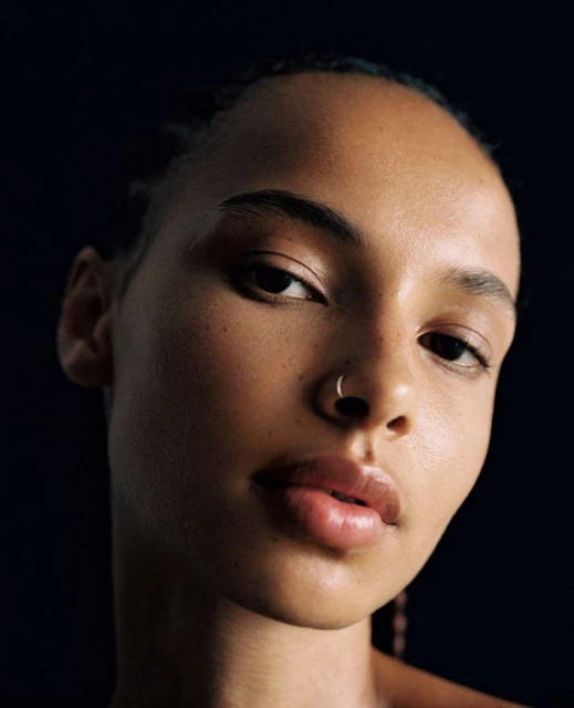 Close-up portrait of a young adult female with dark hair, dark eyes, and smooth skin in a studio setting with dark background.