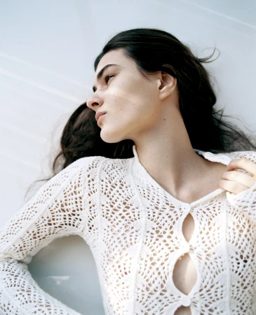 Close-up portrait of a woman wearing a white crochet button-down top against a bright white background