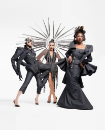 Three models wearing avant-garde dark denim outfits and dramatic headpieces posing against a white seamless background.