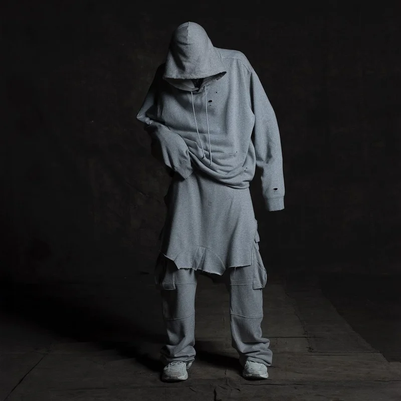 A person standing against a dark background, wearing an oversized grey hoodie and matching cargo pants.