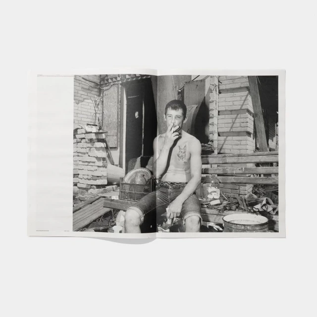 Black and white photo of shirtless man smoking cigarette in dilapidated urban setting with brick walls and debris in open book.