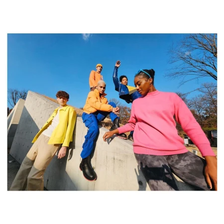 Five young people in brightly colored clothing pose on a concrete structure against a blue sky, showcasing outdoor fashion.
