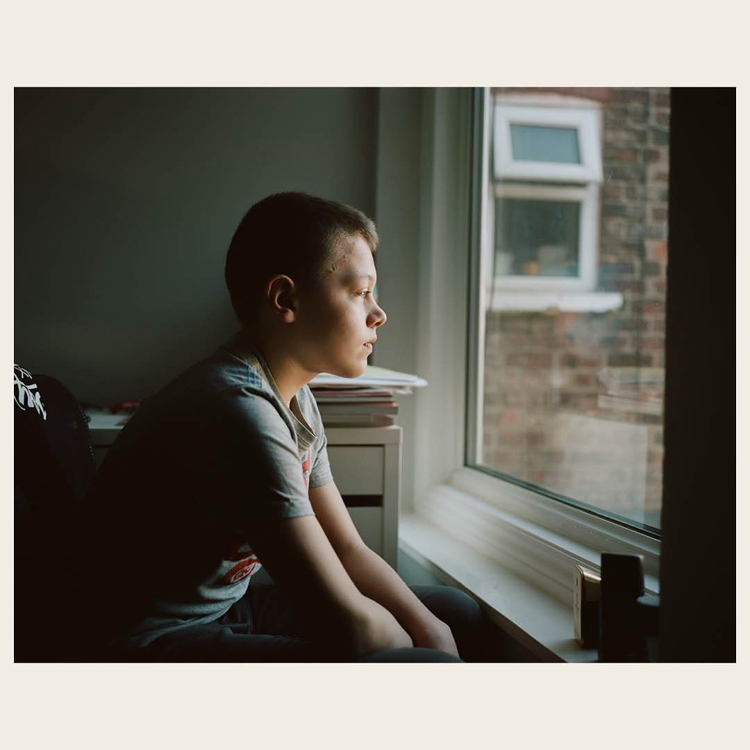 Portrait of a young boy looking out a window in natural daylight, captured with a shallow depth of field. Soft, desaturated colors.