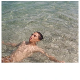 Young man floating peacefully on his back in clear shallow turquoise ocean water with ripples casting light patterns.