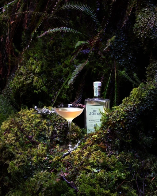 Botanical gin and a cocktail glass sit on moss in a forest setting, presented in a visually rich and captivating display.