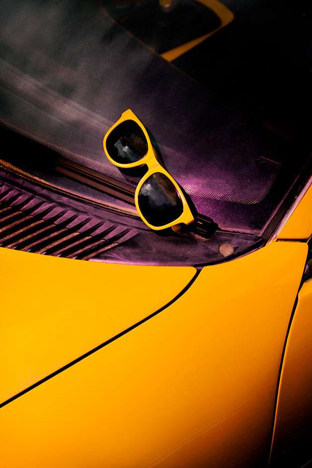 Bright yellow sunglasses are perched on the black dashboard of a vibrant yellow car, close-up shot, providing a bold, sunny contrast.