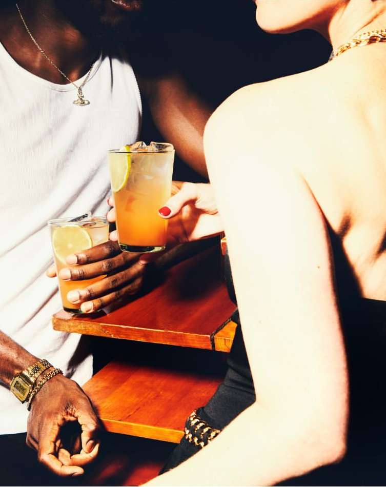 Close-up of an African-American man and a Caucasian woman holding cocktails at a bar, showcasing fashion jewelry and wristwatches.