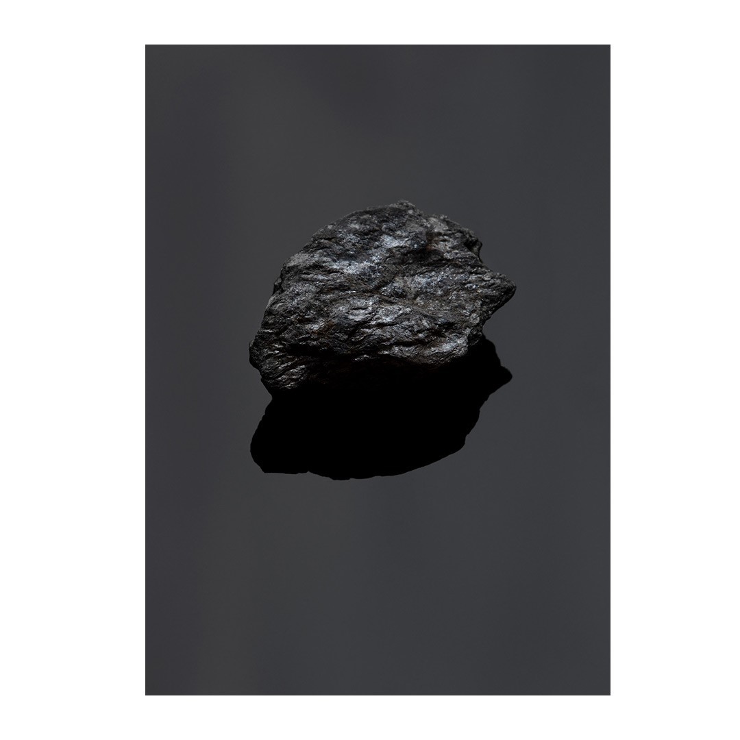 High-contrast studio shot of a single lump of coal reflecting light against a dark background, showcasing its texture and form.