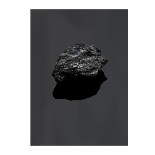 High-contrast studio shot of a single lump of coal reflecting light against a dark background, showcasing its texture and form.