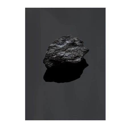 High-contrast studio shot of a single lump of coal reflecting light against a dark background, showcasing its texture and form.